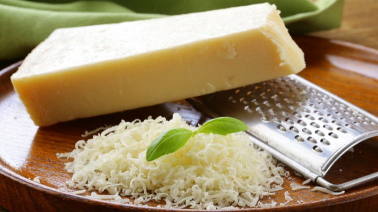A piece of parmesan cheese, a grater and some grated cheese.